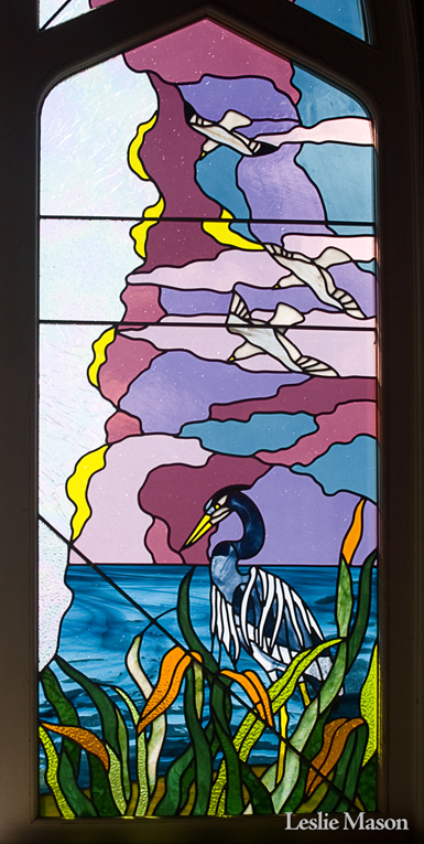 full window with blue heron at the bottom and seagulls flying across a purple sky