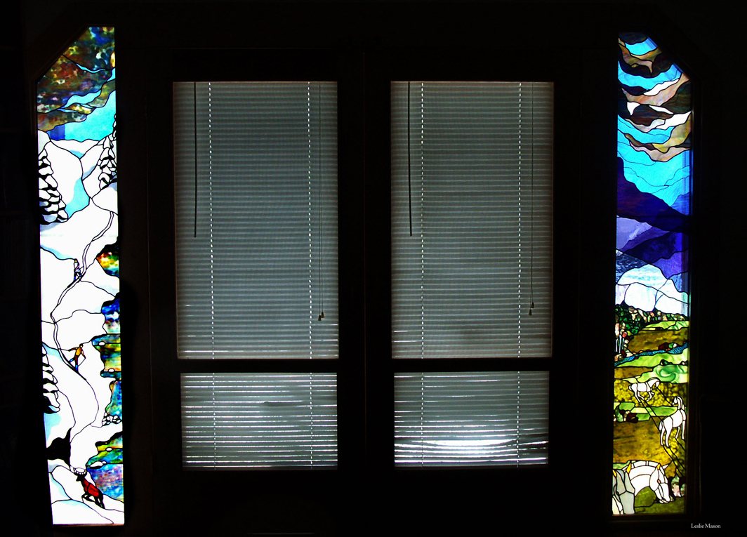 two tall windows, the left with a deer at the bottom of a snowy hill, the right with horses grazing under a dark blue sky