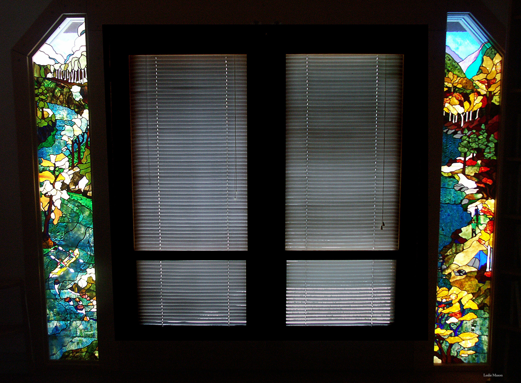two tall windows, the left a river running through a forest and the right a forest at the edge of a lake